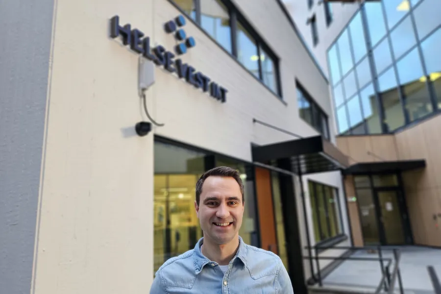 Mann med blå skjorte og mørkt kort hår står utenfor Helse Vest IKT sitt hovedbygg