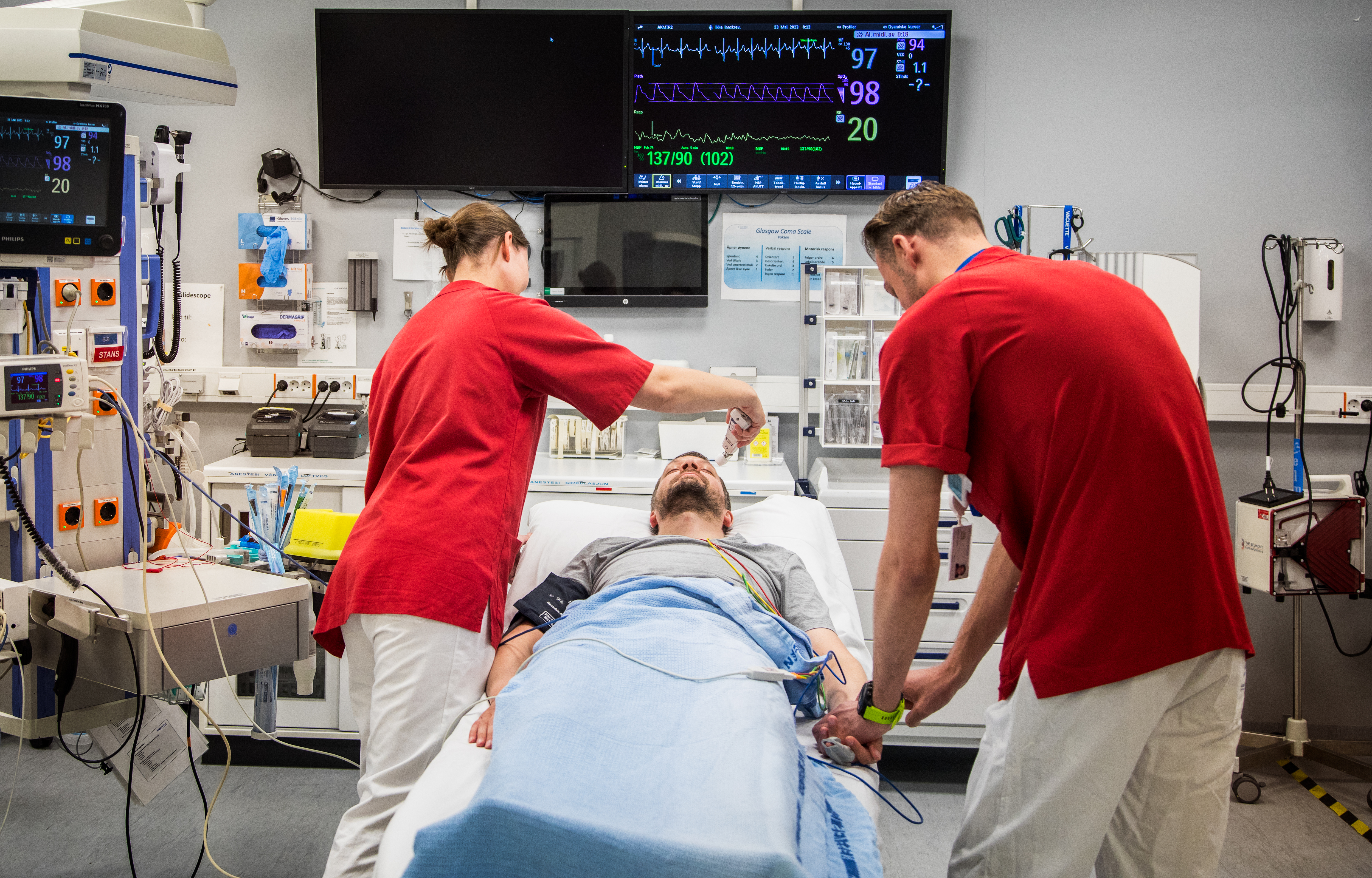 Man ligg i sjukehusseng og får hjelp av medisinsk personal