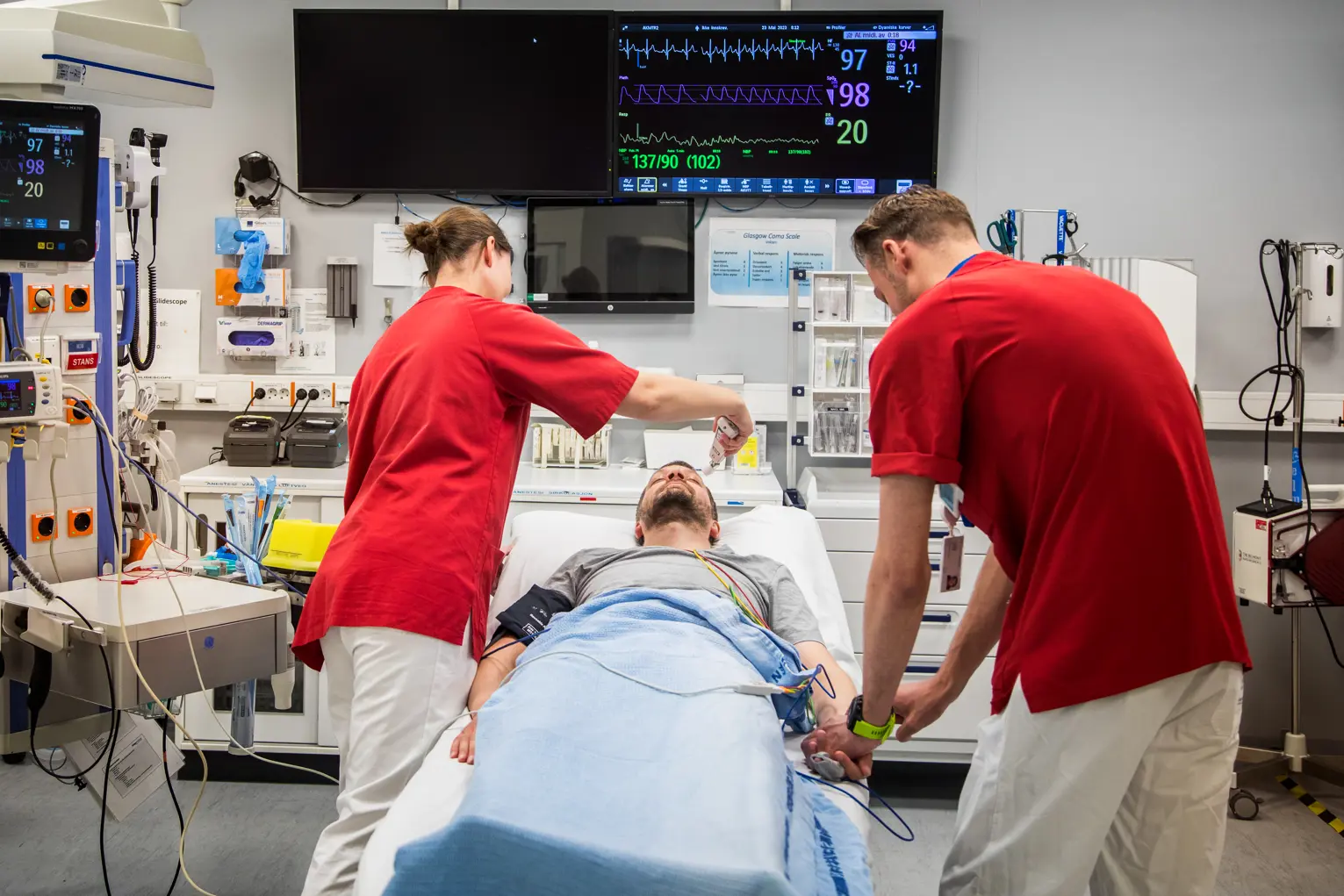 To behandlere står bøyd over pasient i sykeseng