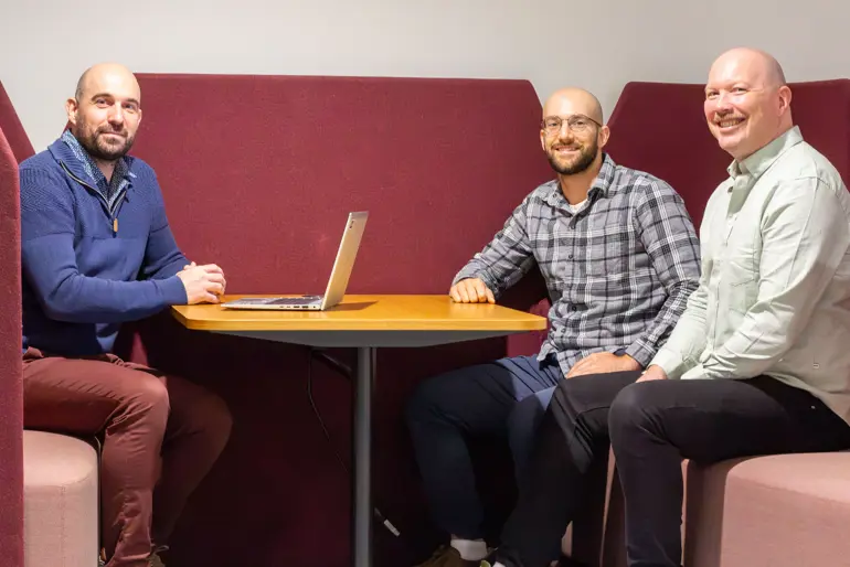 En gruppe menn som sitter ved et bord med en bærbar datamaskin