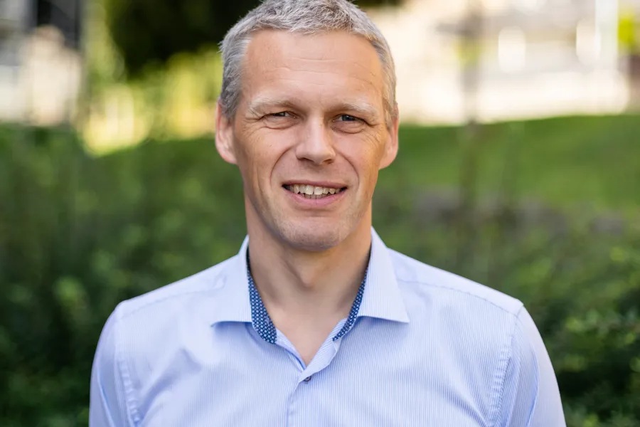 Mann med grått hår og blå skjorte smiler til kamera